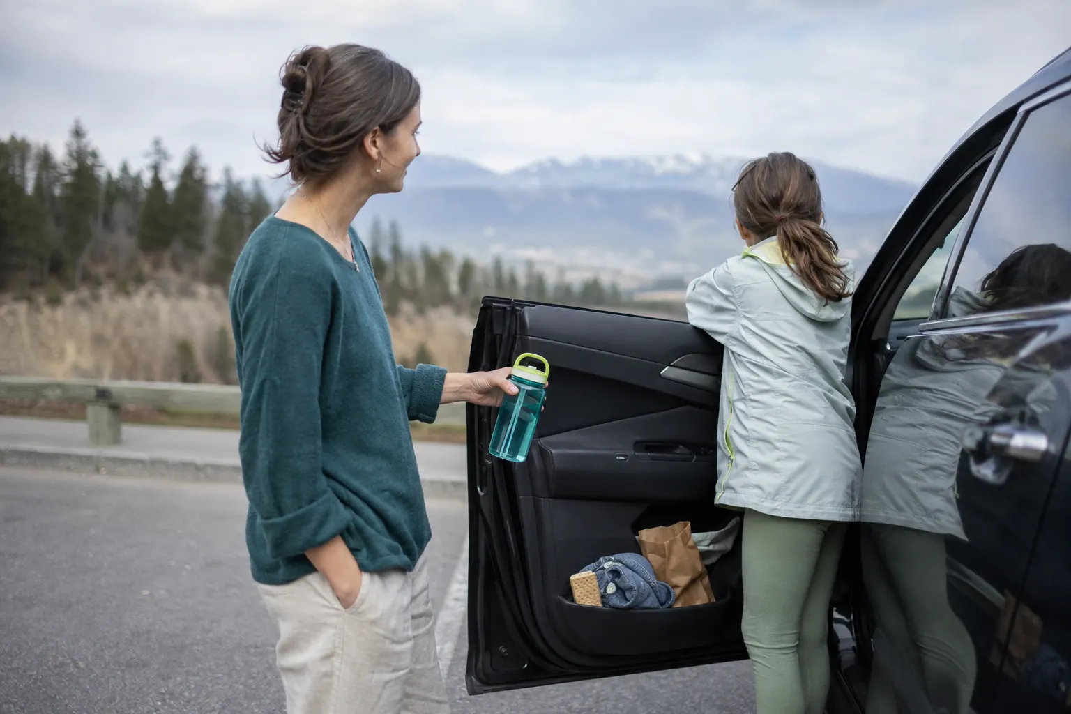 Family taking a roadside break with fresh air, water and plain snacks during a long car trip.
