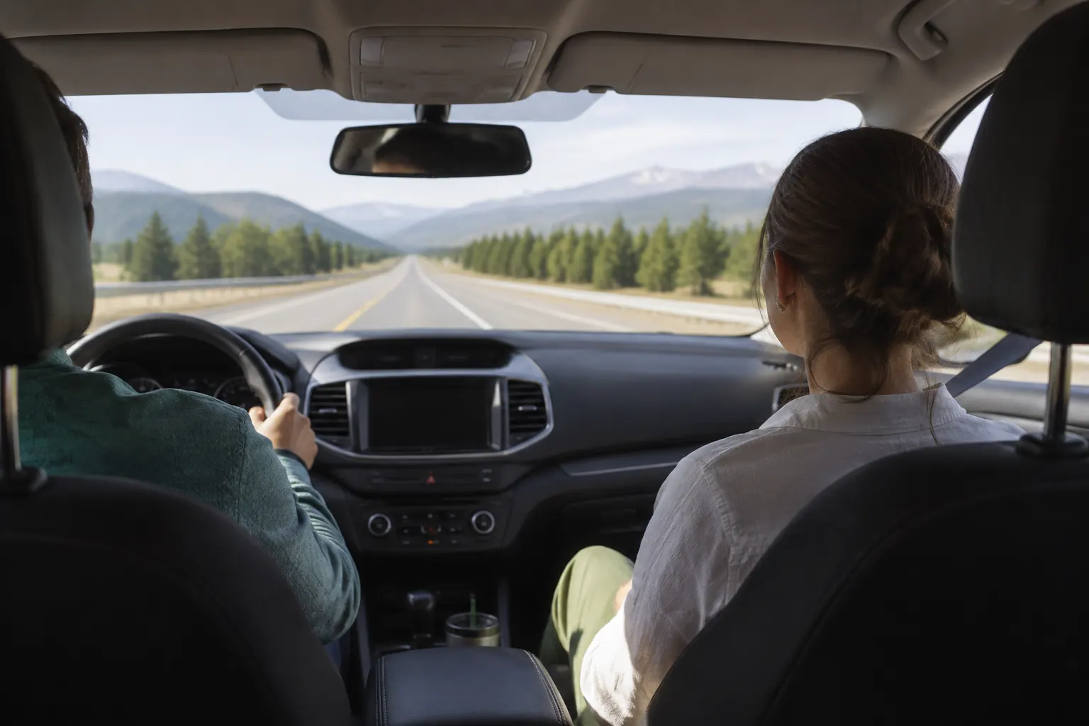 Belted front-seat passenger looking through the windshield toward a distant road and level horizon.
