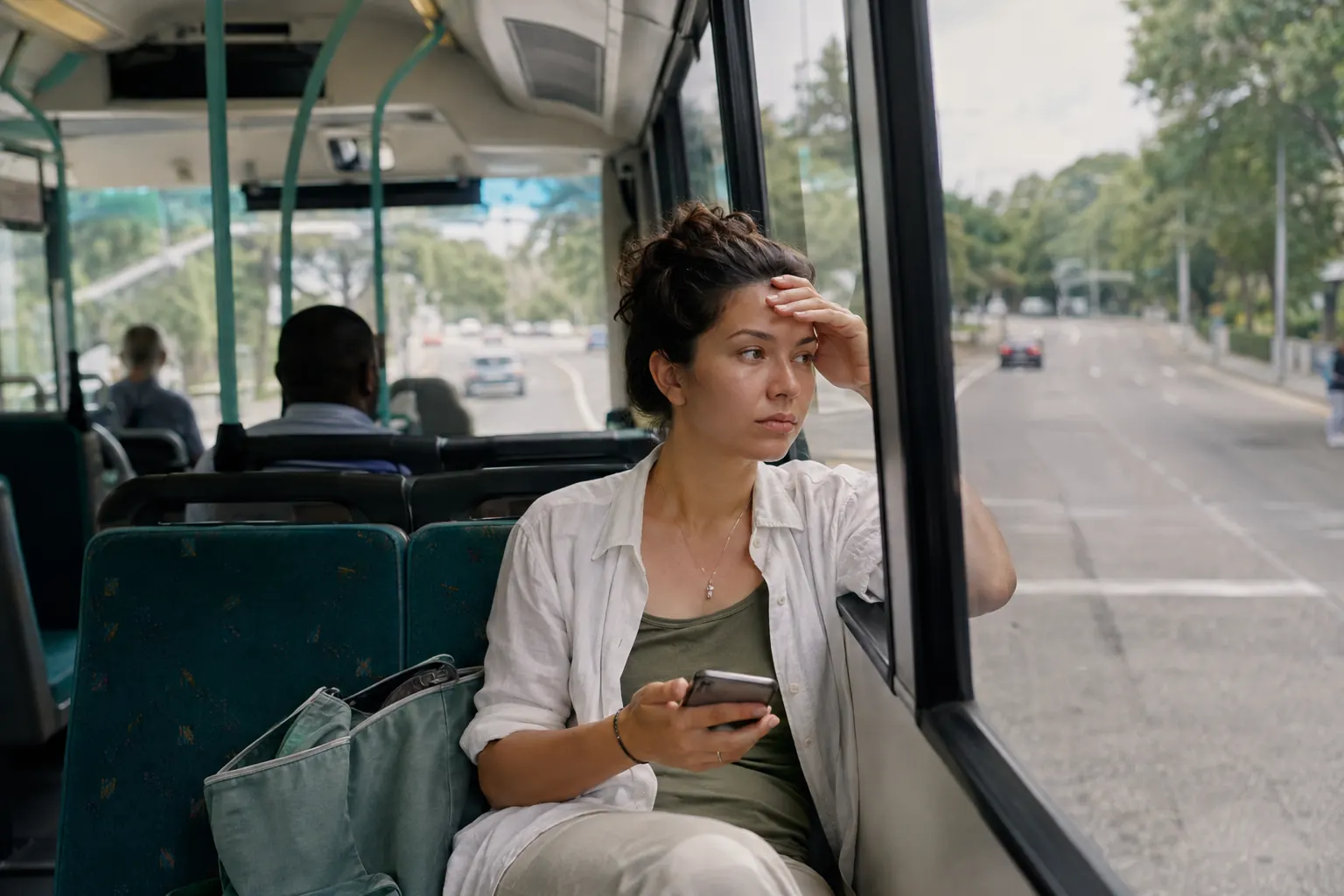 Bus passenger lowering a phone and looking toward the road after noticing an early motion-sickness warning.