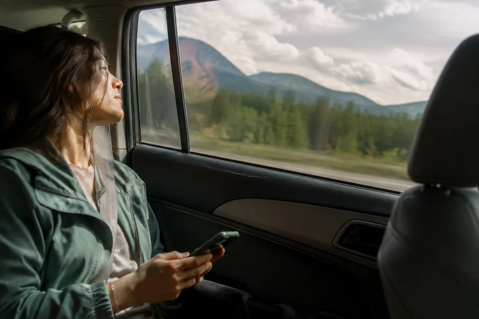 Car passenger looking between a still phone and the moving landscape reflected in the window.