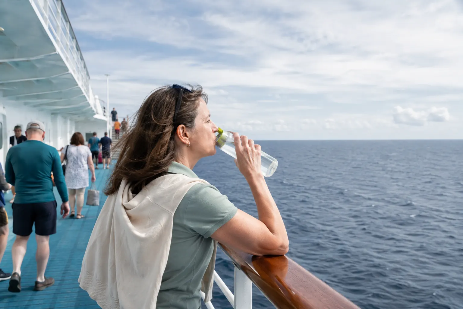 Cruise passenger standing midship on an open deck and looking at the horizon with water nearby.