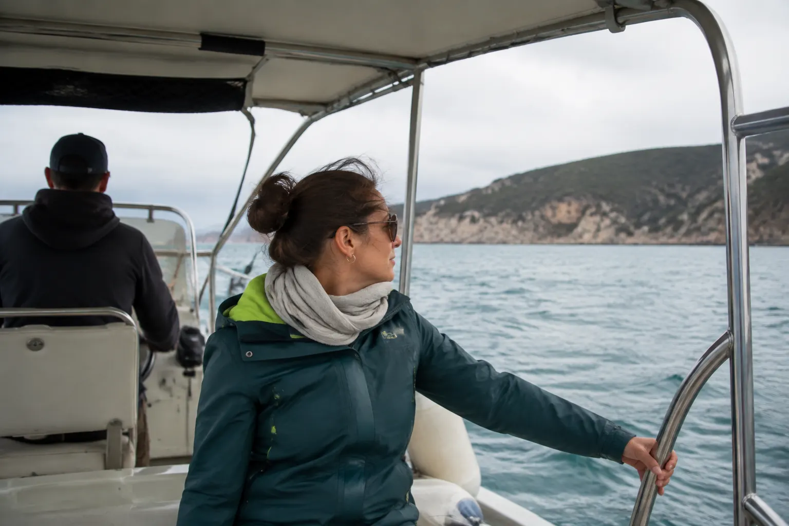 Passenger seated near the center of a small boat beside the helm and facing the horizon.
