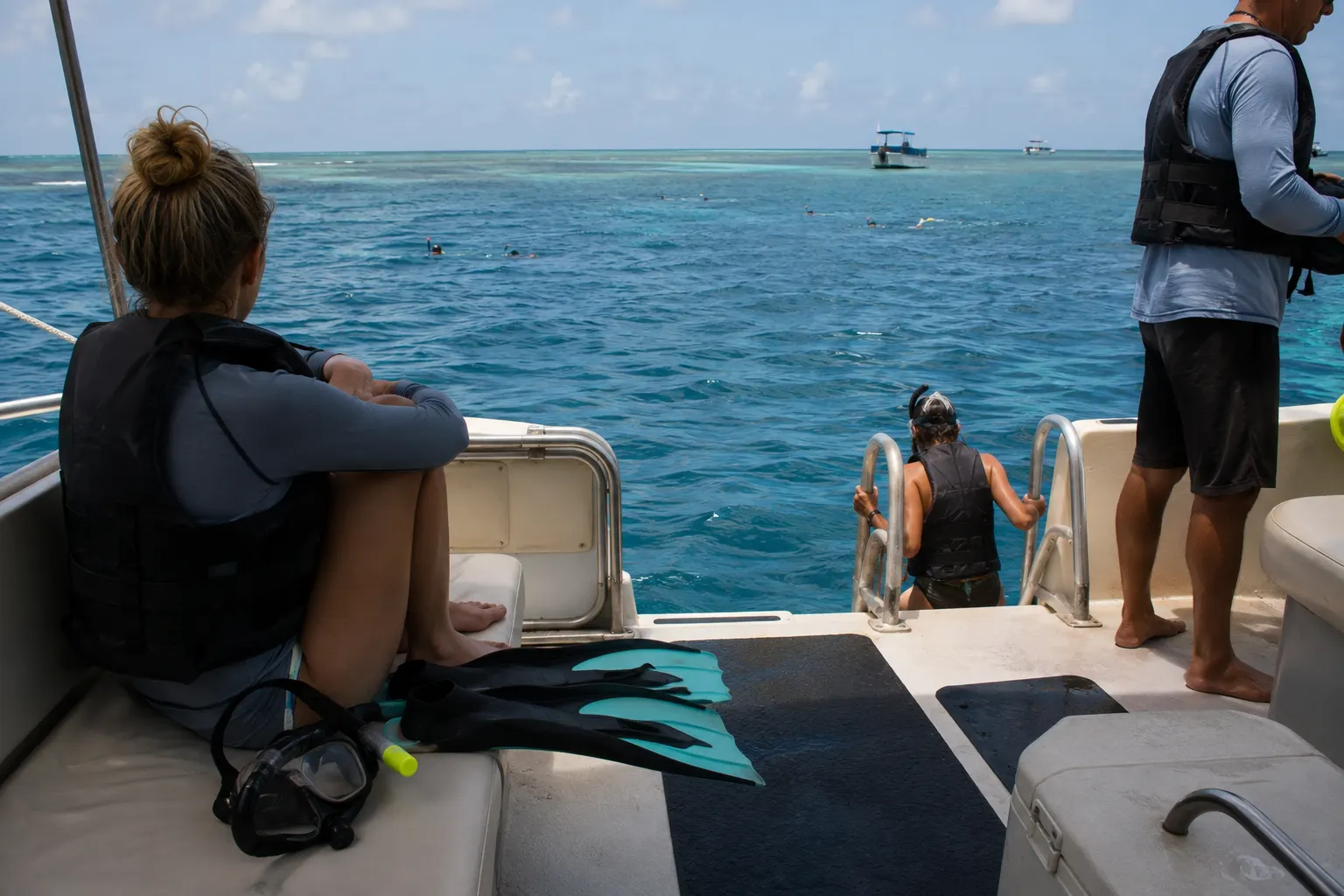 Snorkel-tour guest facing the horizon on a safely moored boat while others prepare to enter the water.