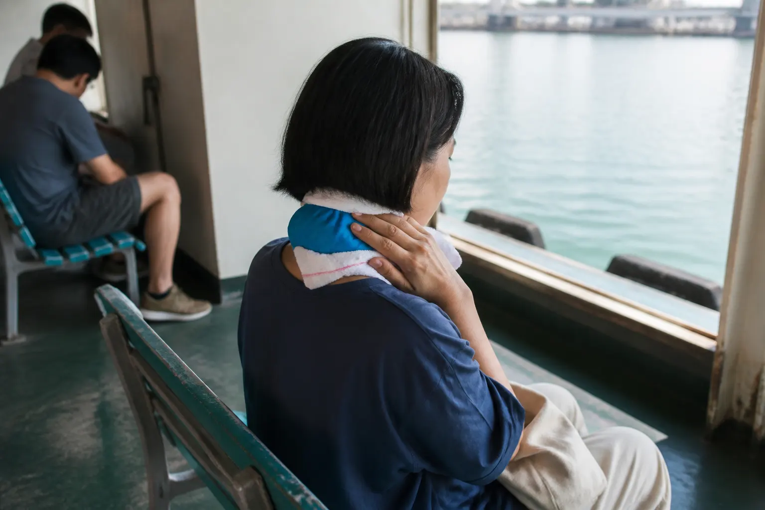 Ferry traveler holding a cloth-wrapped cold pack against the back of their neck while resting.