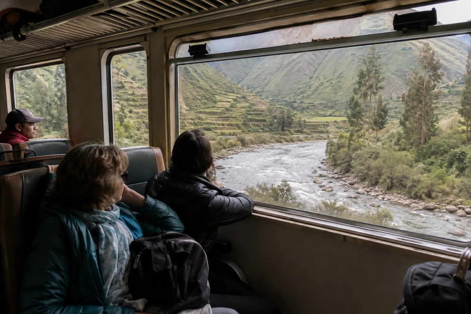 Travelers viewing a river and terraced slopes from an unbranded train in Peru's Sacred Valley.