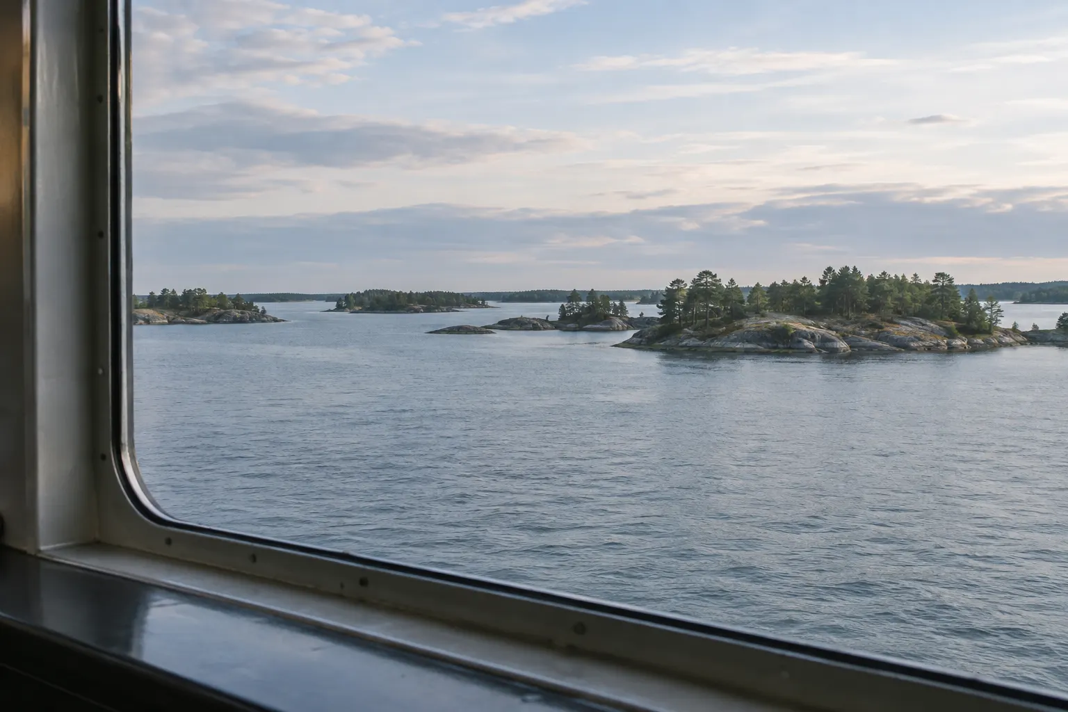 Low wooded islands and gentle ripples seen through a ferry window in sheltered water.