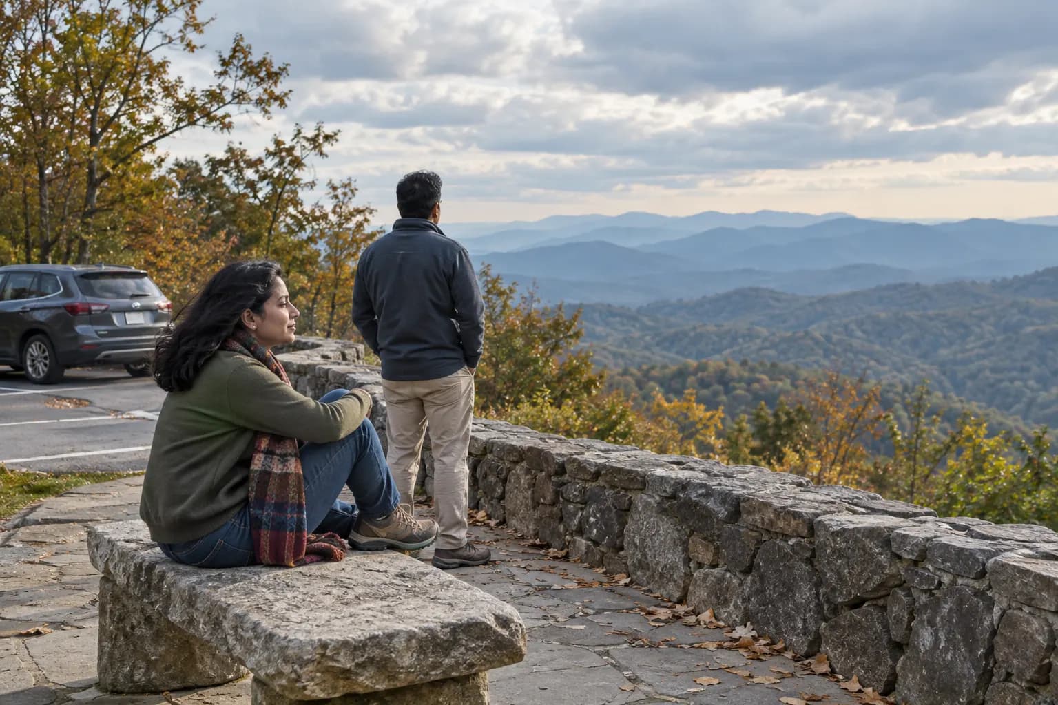 Travelers resting at a paved mountain overlook with forested ridges in the distance.