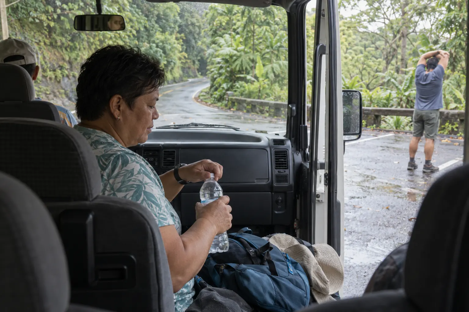 Minibus passenger taking a water break at a designated stop beside a winding tropical road.