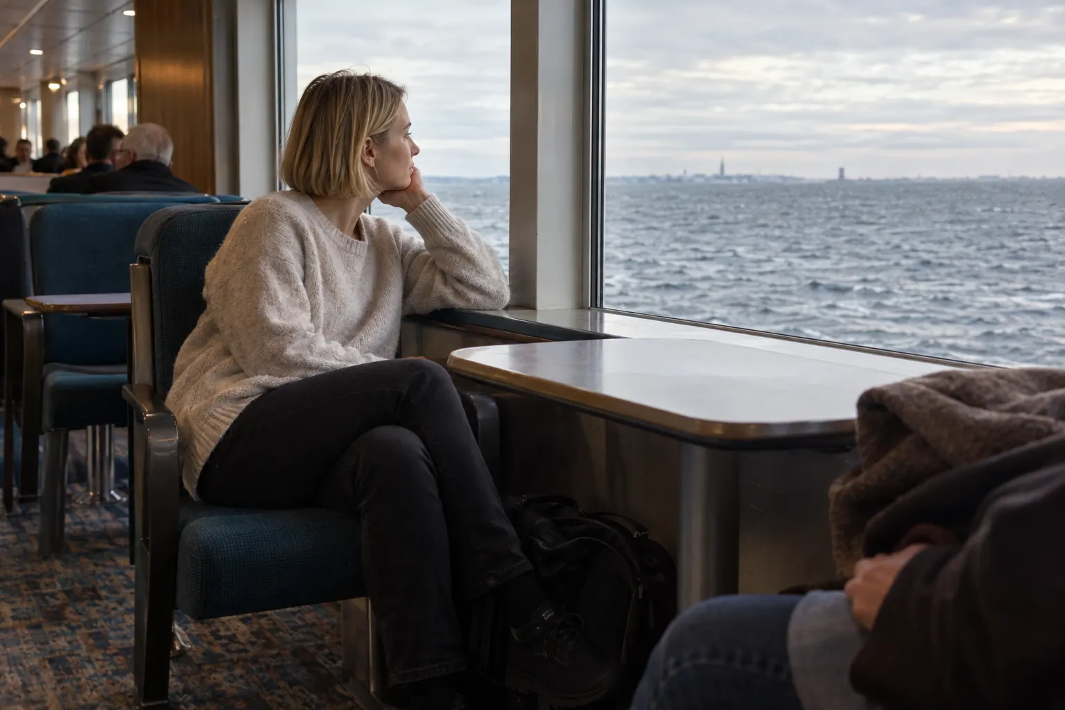 Traveler seated in a ferry lounge and watching the horizon through a broad window.