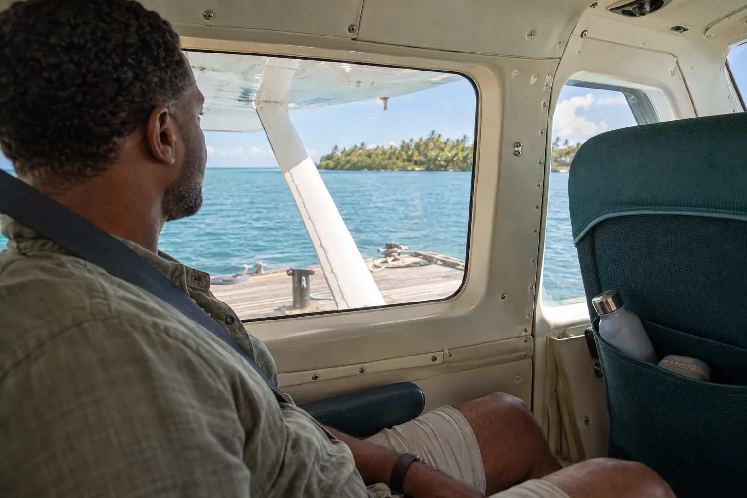Seated floatplane passenger looking across the lagoon while the aircraft waits at a floating dock.