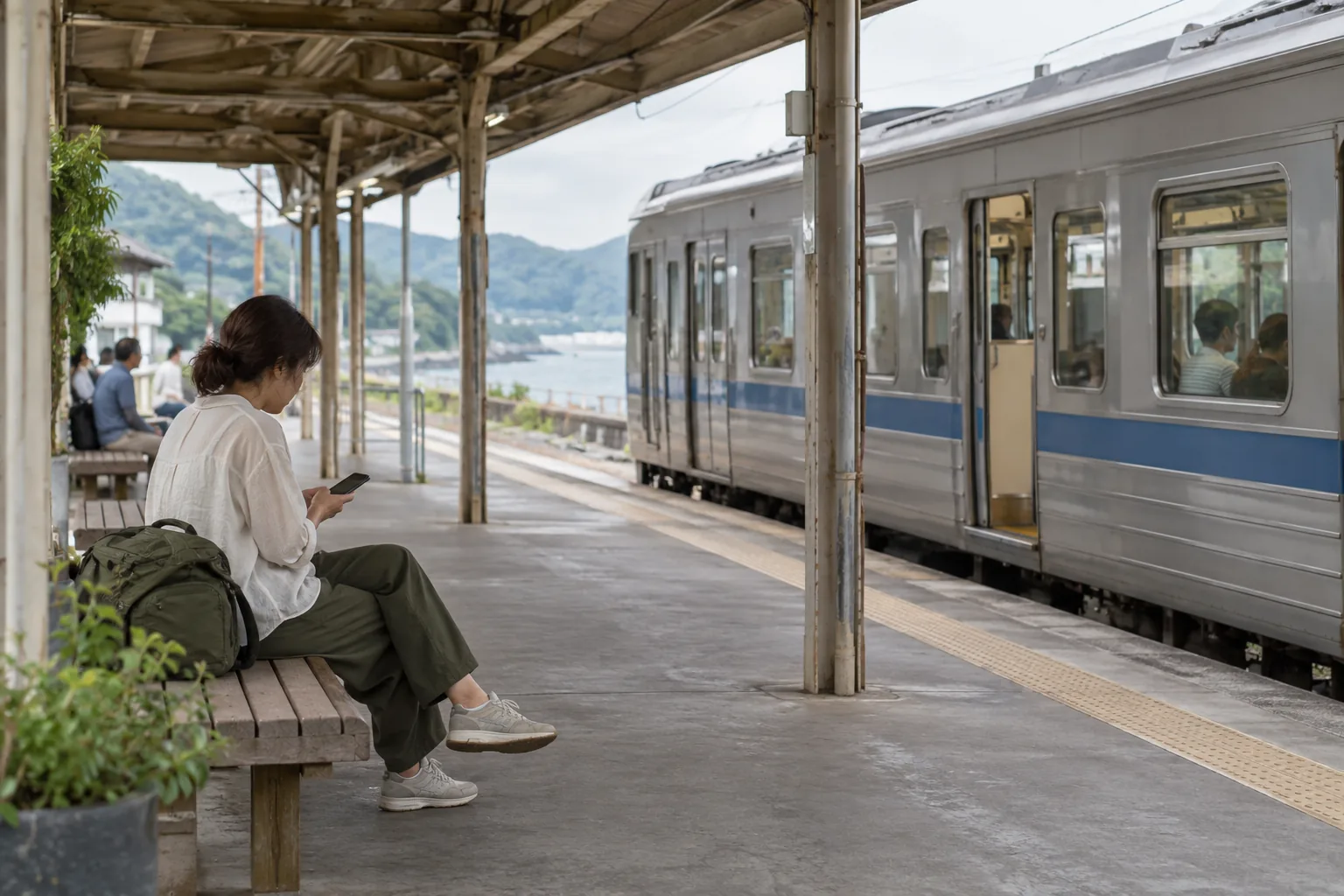 Traveller checking a phone from a station bench while a train waits motionless beside the platform.