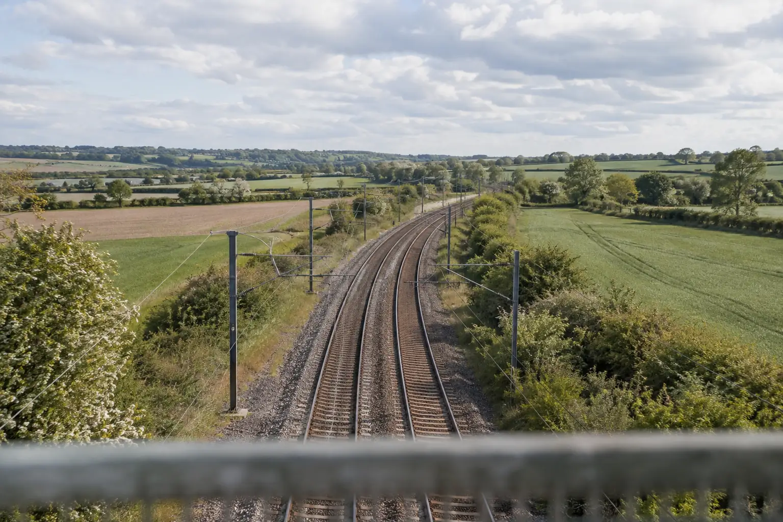 A railway following a broad gentle curve across open countryside, viewed from a safe public footbridge.