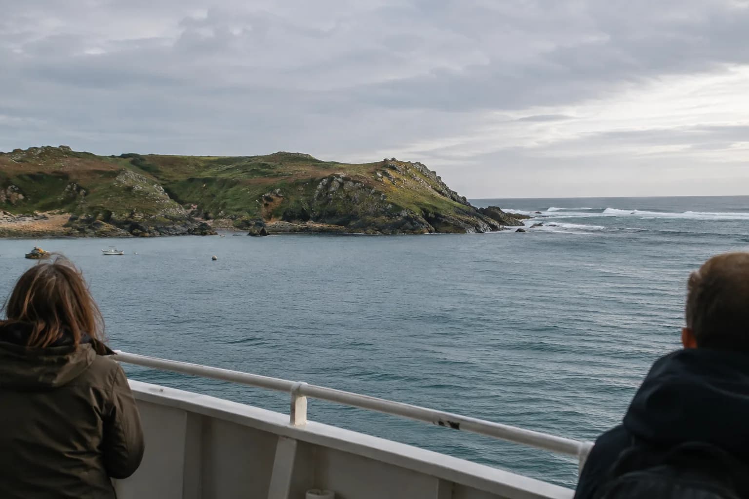 A sheltered coastal bay giving way to open ocean beyond a low headland, viewed from a passenger deck.