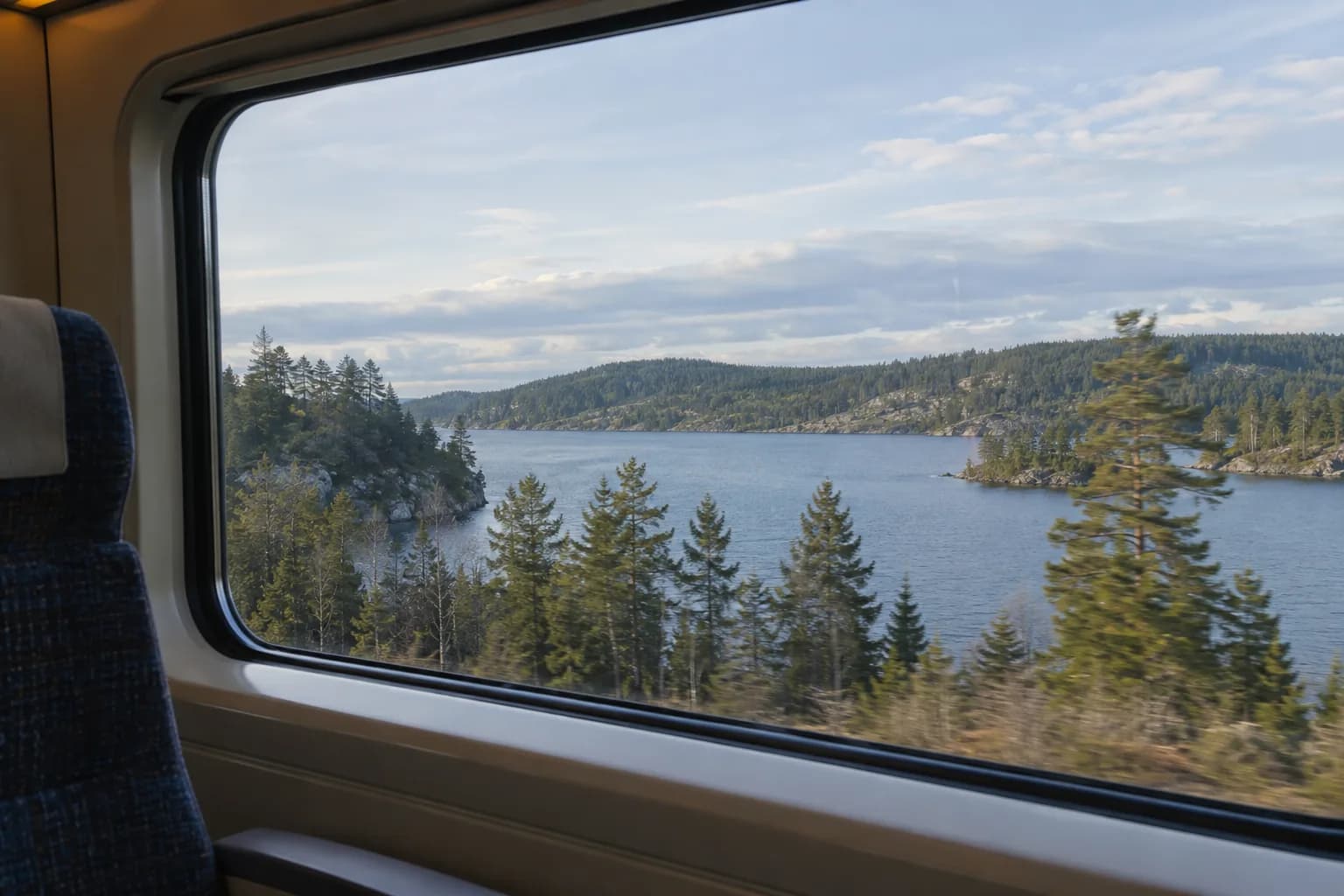 Lake and pine forest visible through a train window beside an ordinary passenger seat.