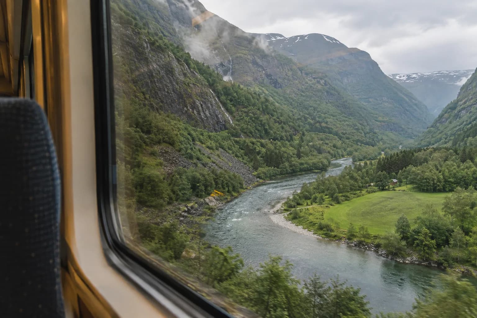 A river and steep green valley seen through a train window during a mountain descent.