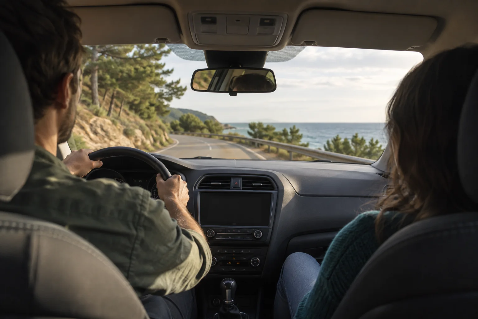Front passenger looking ahead through the windscreen toward a coastal road bend.