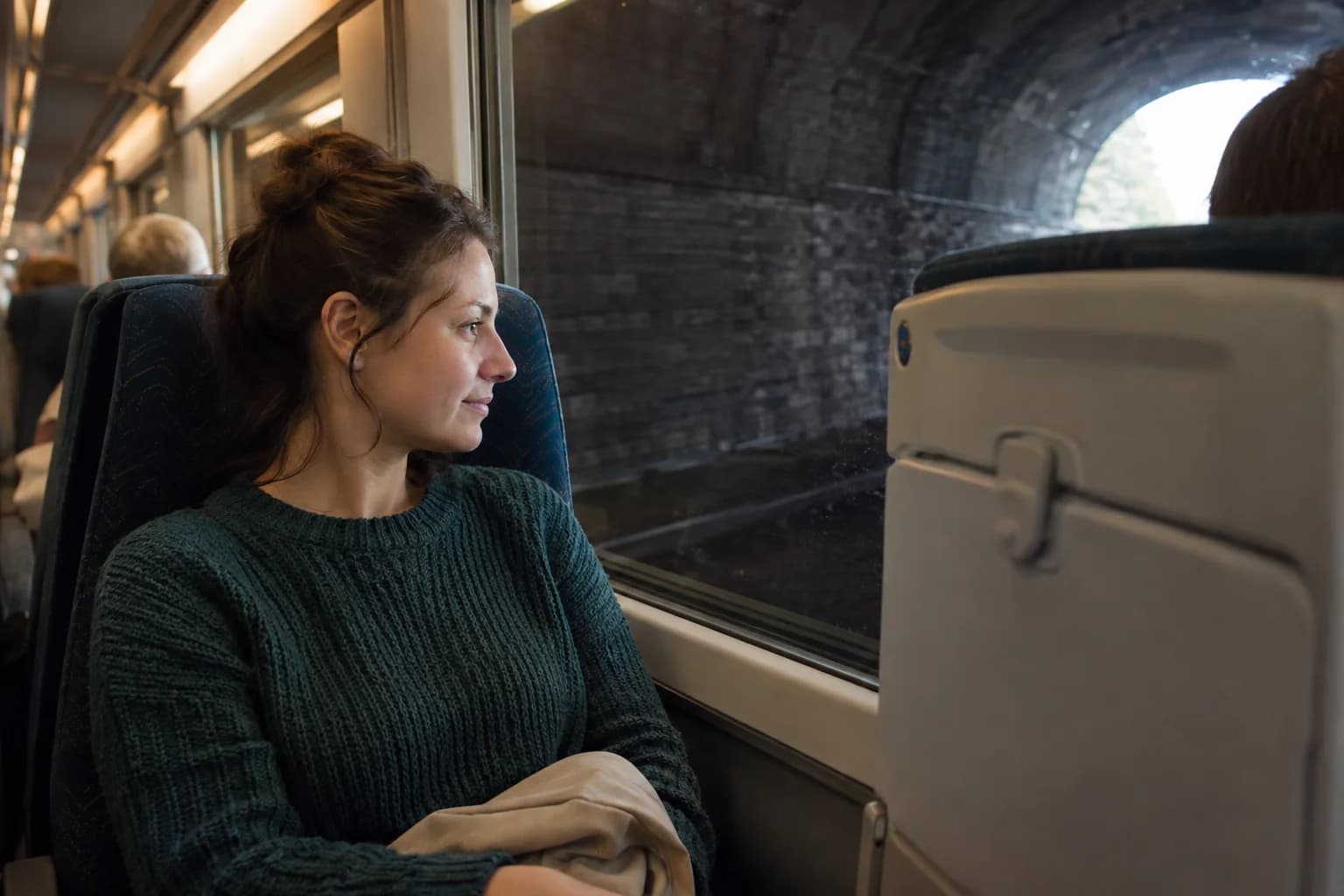 Passenger looking toward a still seatback while the train's side window shows the dark interior of a tunnel.