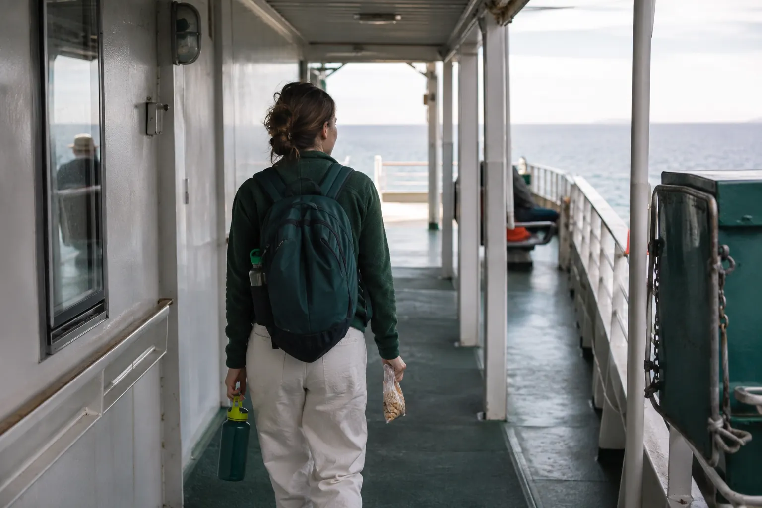 Traveler moving through the middle of a passenger ship toward an open deck with a horizon view.