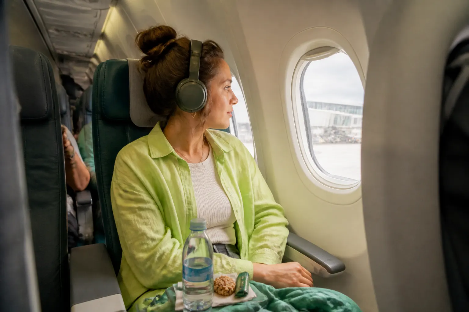 Airline passenger preparing water and headphones in an over-wing window seat before takeoff.