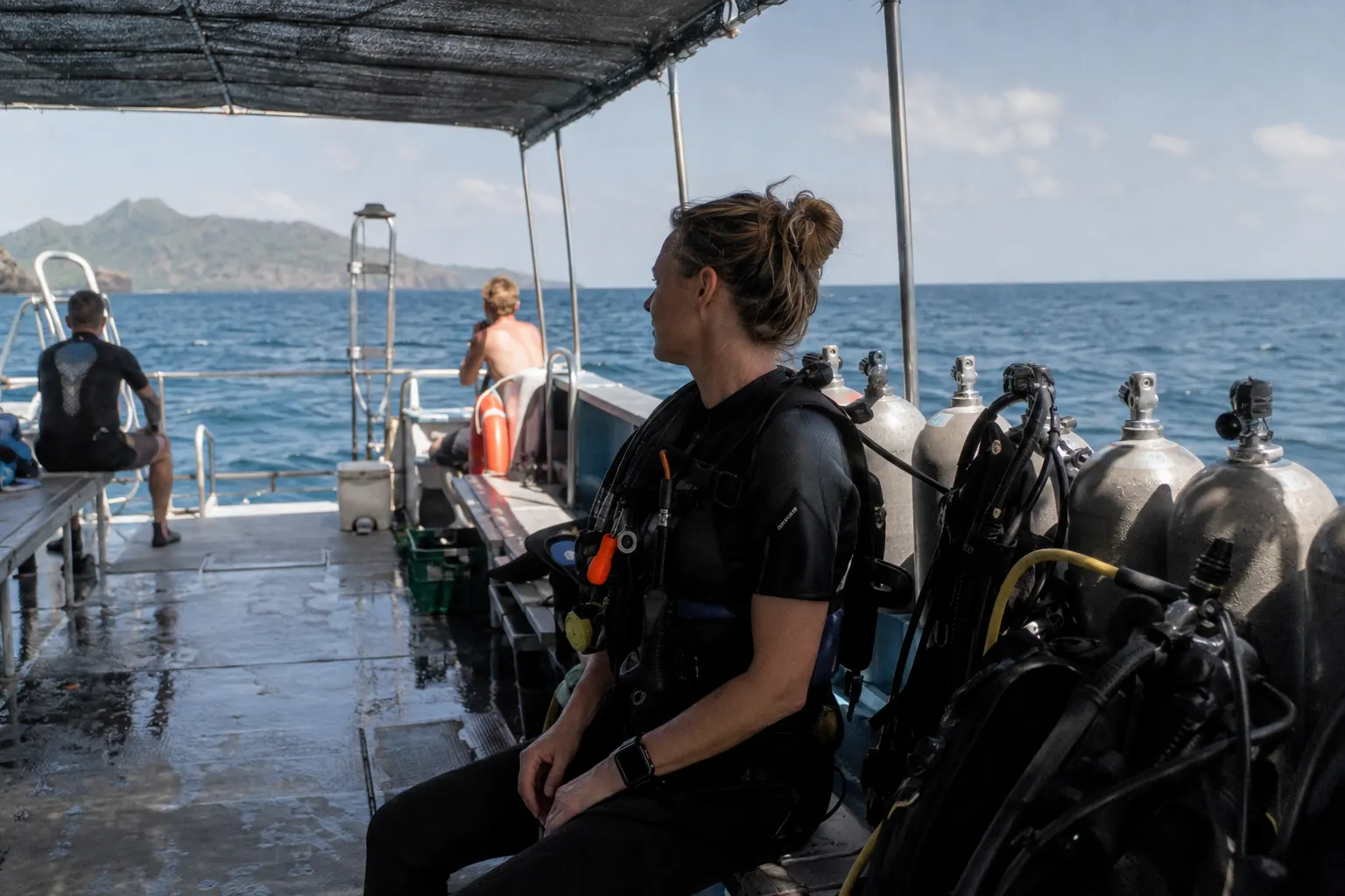 Divers resting safely on a moored dive boat with equipment secured and one person watching the horizon.