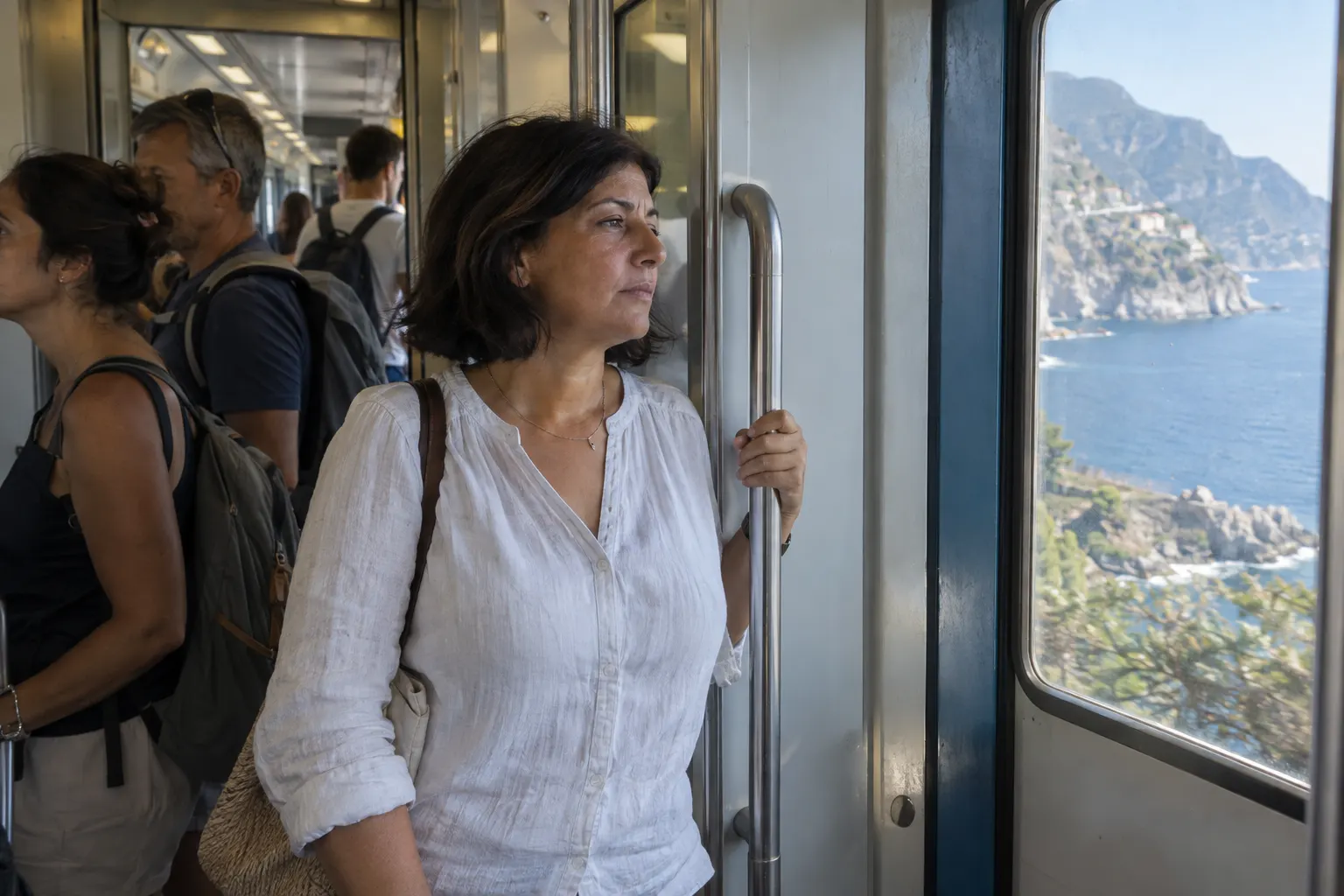 Passenger holding a fixed rail inside a regional train as a coastal view returns beyond a tunnel.