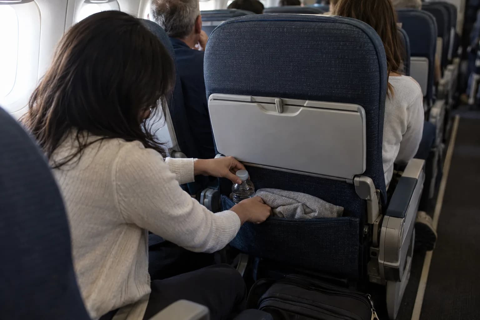 Passenger stowing water and a light layer within reach before a long flight.
