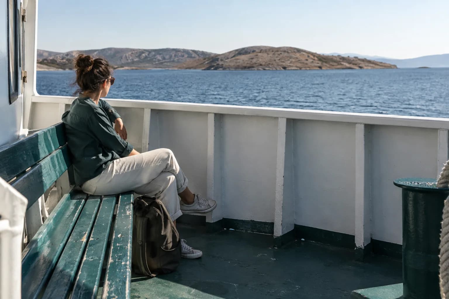 Traveller seated well inside a ferry rail with low dry-climate islands and a distant horizon beyond.