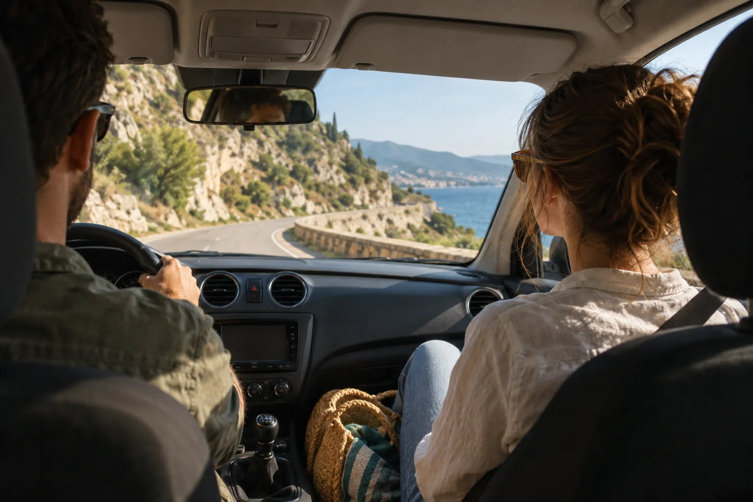 Belted car passenger looking ahead along a narrow coastal road with sea visible beyond the bend.