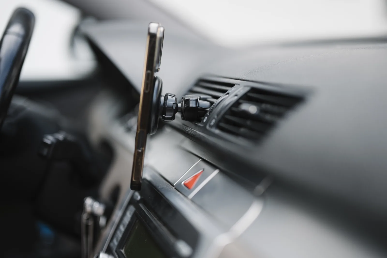 Smartphone mounted beside the air vents on a car dashboard, seen in profile from inside the car in soft daylight.